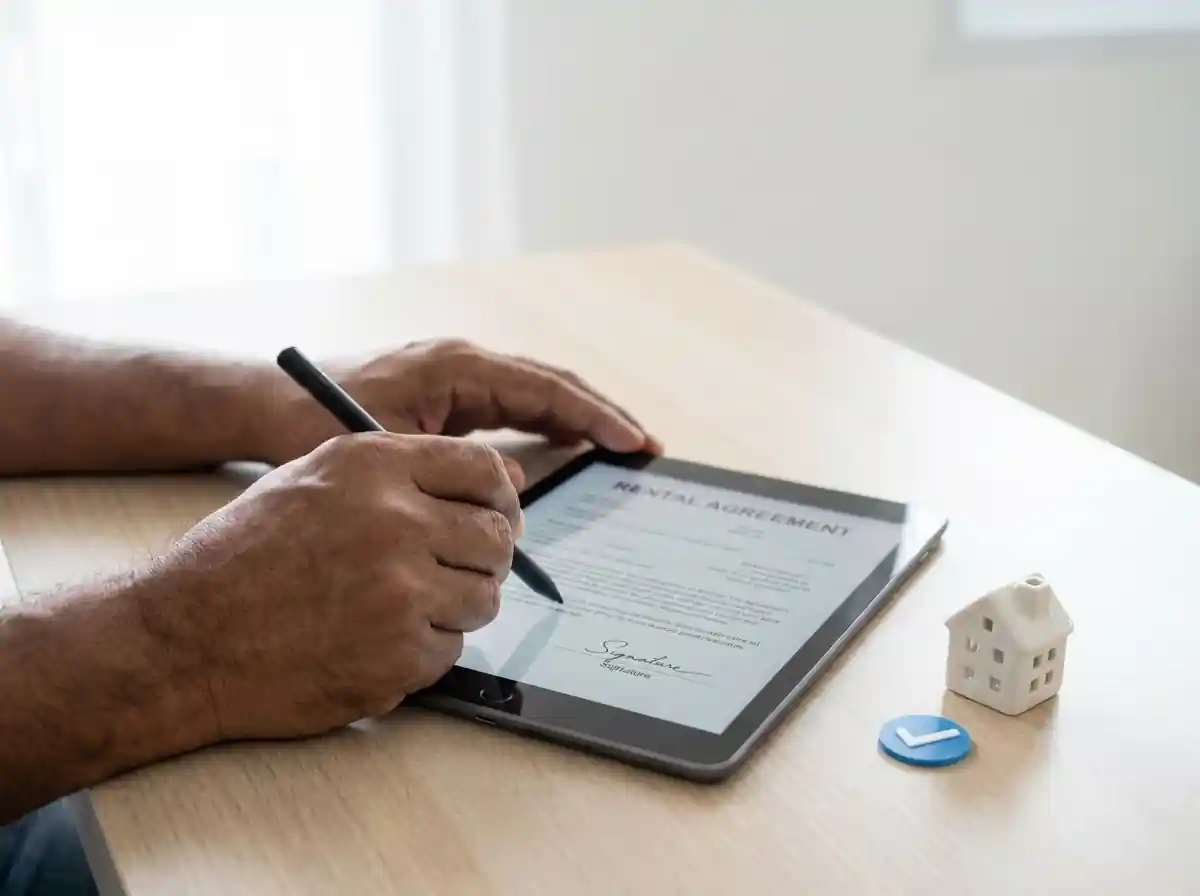 Digital rental agreement being signed on a tablet for NRI property in India with house model on desk Digital rental agreement being signed on a tablet for NRI property in India with house model on desk